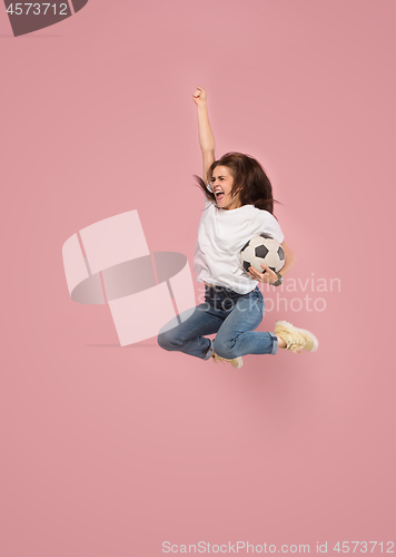 Image of Forward to the victory.The young woman as soccer football player jumping and kicking the ball at studio on pink