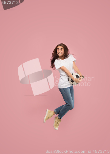 Image of Forward to the victory.The young woman as soccer football player jumping and kicking the ball at studio on pink