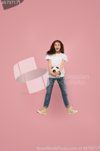 Image of Forward to the victory.The young woman as soccer football player jumping and kicking the ball at studio on pink