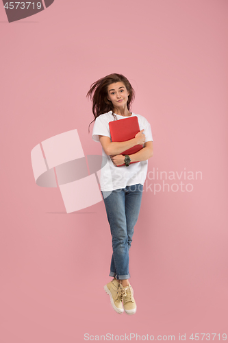 Image of Image of young woman over pink background using laptop computer or tablet gadget while jumping.