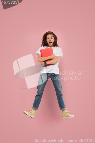 Image of Image of young woman over pink background using laptop computer or tablet gadget while jumping.