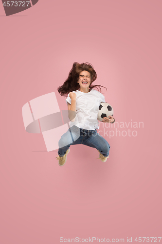 Image of Forward to the victory.The young woman as soccer football player jumping and kicking the ball at studio on pink