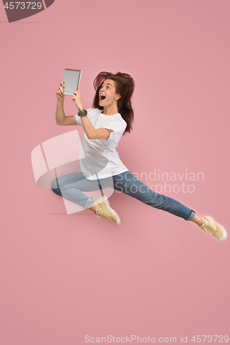 Image of Image of young woman over pink background using laptop computer or tablet gadget while jumping.