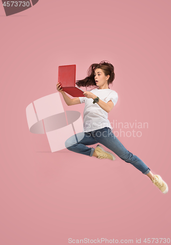 Image of Image of young woman over pink background using laptop computer or tablet gadget while jumping.