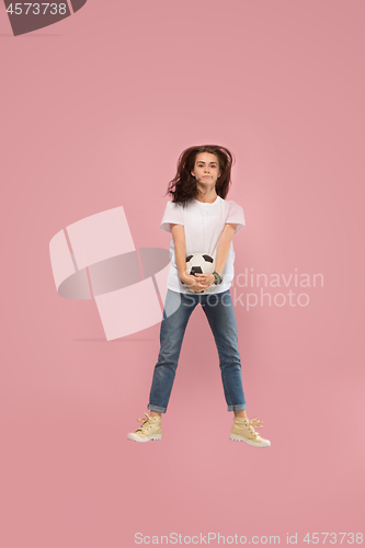 Image of Forward to the victory.The young woman as soccer football player jumping and kicking the ball at studio on pink