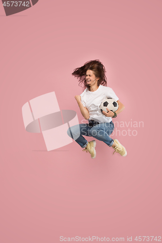 Image of Forward to the victory.The young woman as soccer football player jumping and kicking the ball at studio on pink