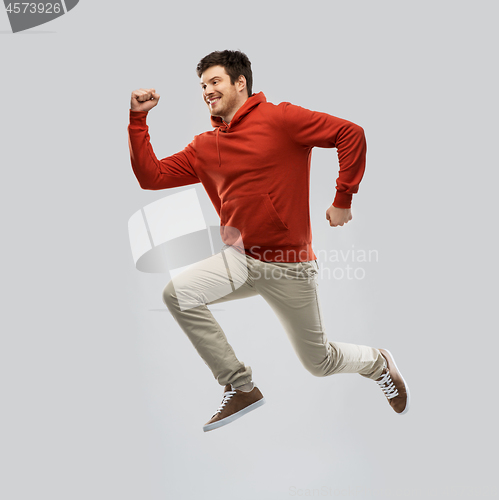 Image of young man in hoodie jumping over grey background