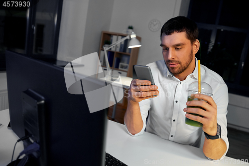 Image of businessman with drink using smartphone at office