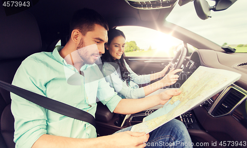 Image of happy man and woman with road map driving in car