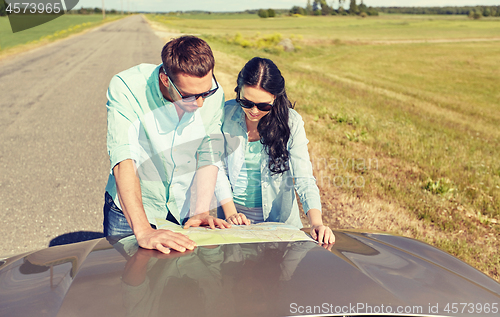 Image of happy man and woman with road map on car hood