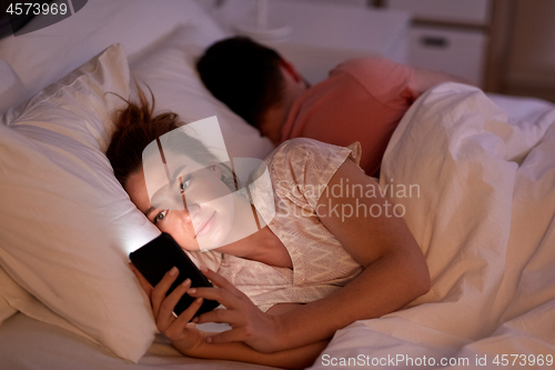 Image of woman using smartphone while boyfriend is sleeping