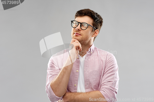 Image of thinking young man in glasses over grey background