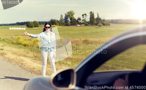 Image of woman hitchhiking and stopping car at countryside