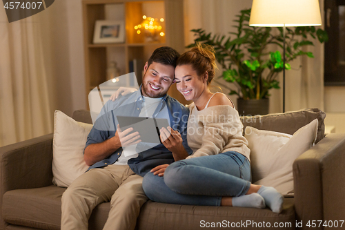 Image of happy couple using tablet pc at home in evening