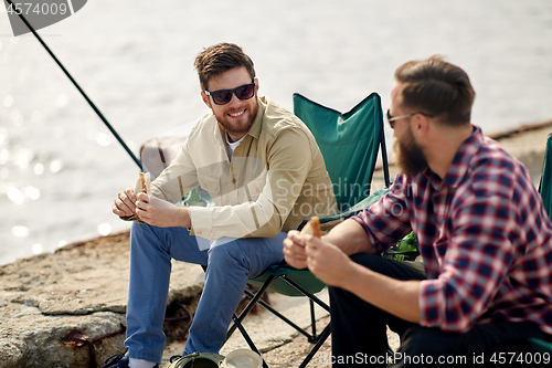 Image of happy friends fishing and eating sandwiches