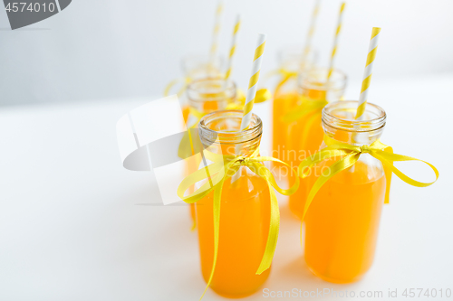 Image of orange juice in glass bottles with paper straws