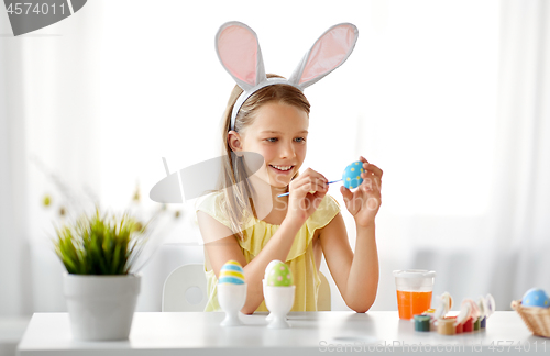 Image of happy girl coloring easter eggs at home