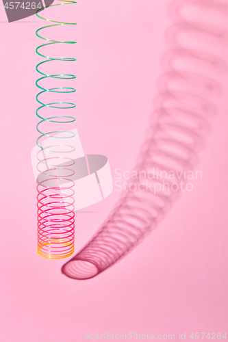 Image of Vertical stretching plastic slinky toy with curved shadow.