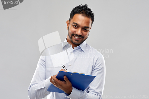 Image of smiling indian businessman writing to clipboard