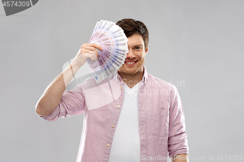 Image of smiling young man with fan of euro money over grey