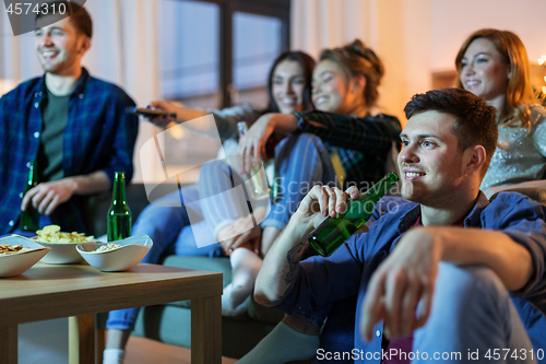 Image of happy friends with drinks watching tv at home