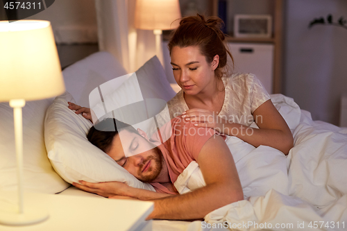 Image of woman wakes her sleeping husband up in bed at home