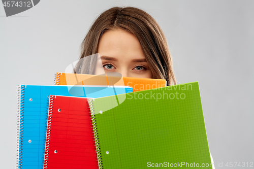 Image of teenage student girl hiding behind notebooks