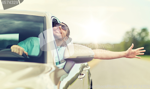 Image of happy man in shades driving car and waving hand