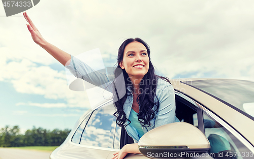 Image of happy young woman driving in car and waving hand
