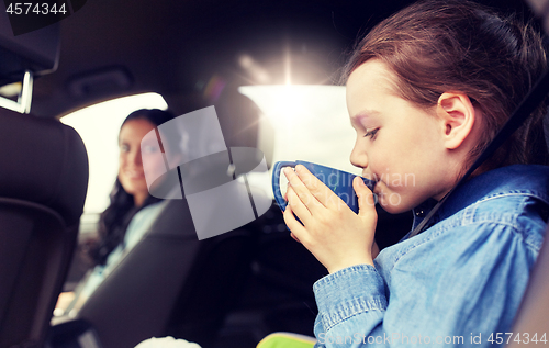 Image of little girl driving in car and drinking from cup