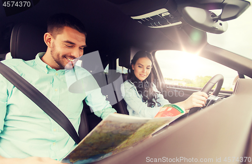 Image of happy man and woman with road map driving in car