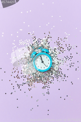 Image of Alarm clock with twelve hours on a holiday background with silver glitter.