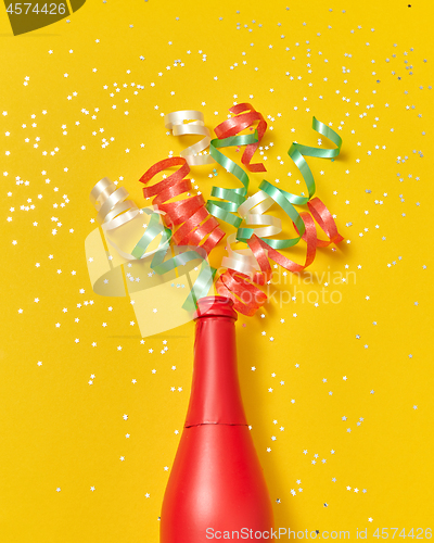 Image of Colorful paper spirals as a champagne bubbles foam from red painted bottle.