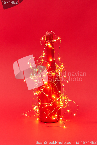 Image of Painted red wine bottle covered Christmas garland with lights.