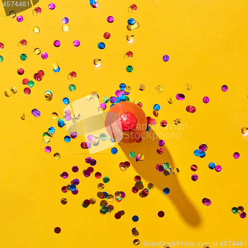 Image of Top view of red painted bottle with confetti on yellow.