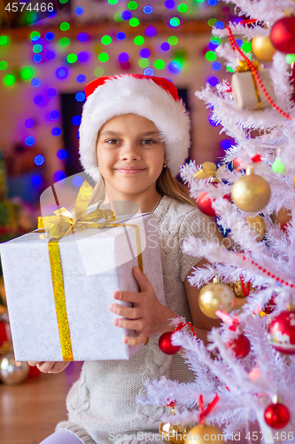Image of Girl sitting by the Christmas tree with big gifts in her hands