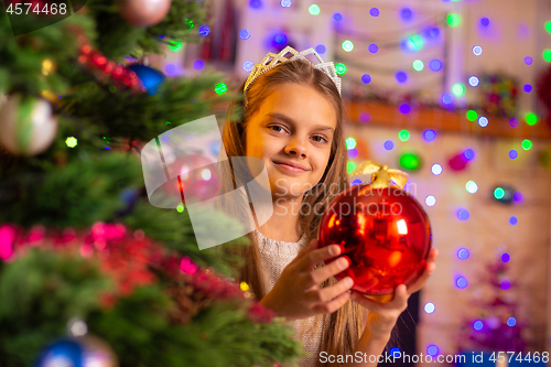 Image of Beautiful ten year old girl peeking out with a big red ball from behind a Christmas tree