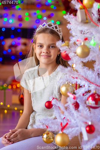 Image of Beautiful girl sits by a white Christmas tree