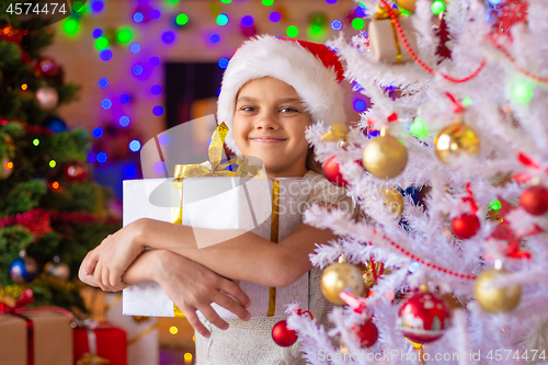 Image of The girl at the Christmas tree holds a big gift in her hands