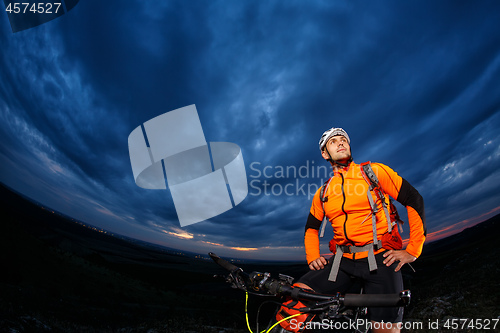 Image of cyclist standing with mountain bike on trail at sunset