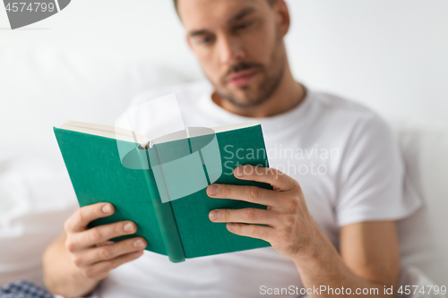 Image of close up of man in bed reading book at home