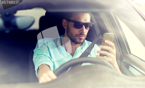 Image of man in sunglasses driving car with smartphone