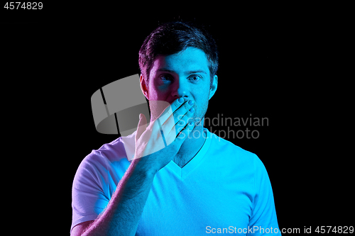 Image of man covering his mouth by hand in neon lights