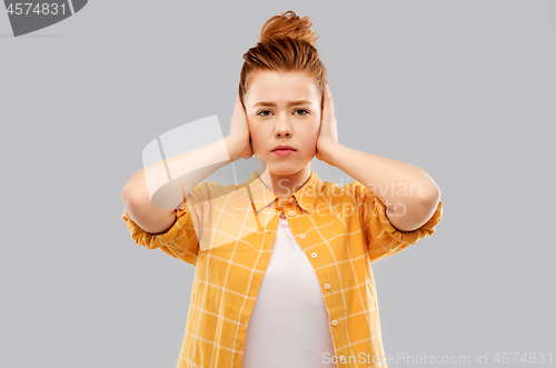 Image of red haired teenage girl closing ears by hands