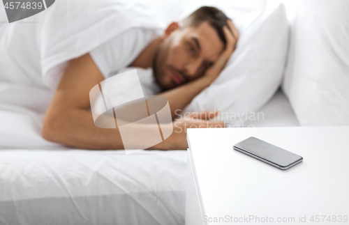 Image of smartphone on bedside table near sleeping man