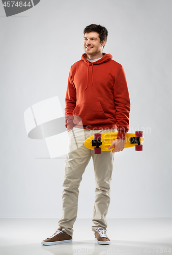 Image of smiling young man in hoodie with short skateboard