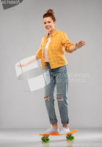 Image of red haired teenage girl riding on short skateboard