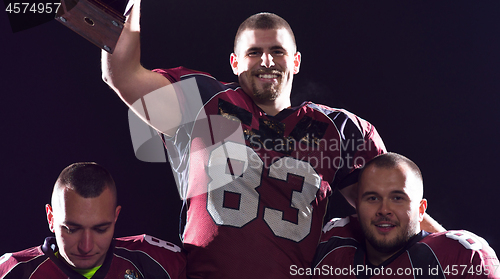 Image of american football team with trophy celebrating victory