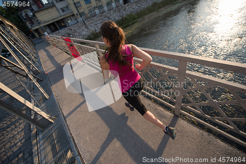 Image of woman jogging across the bridge at sunny morning