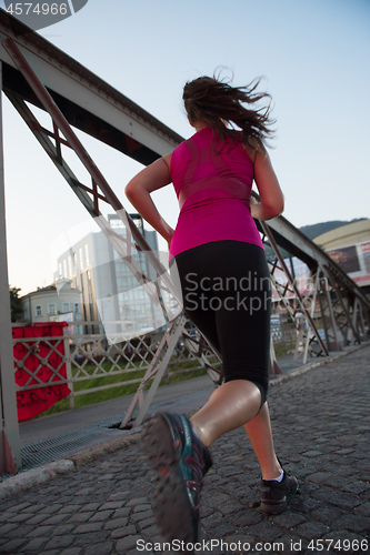 Image of woman jogging across the bridge at sunny morning